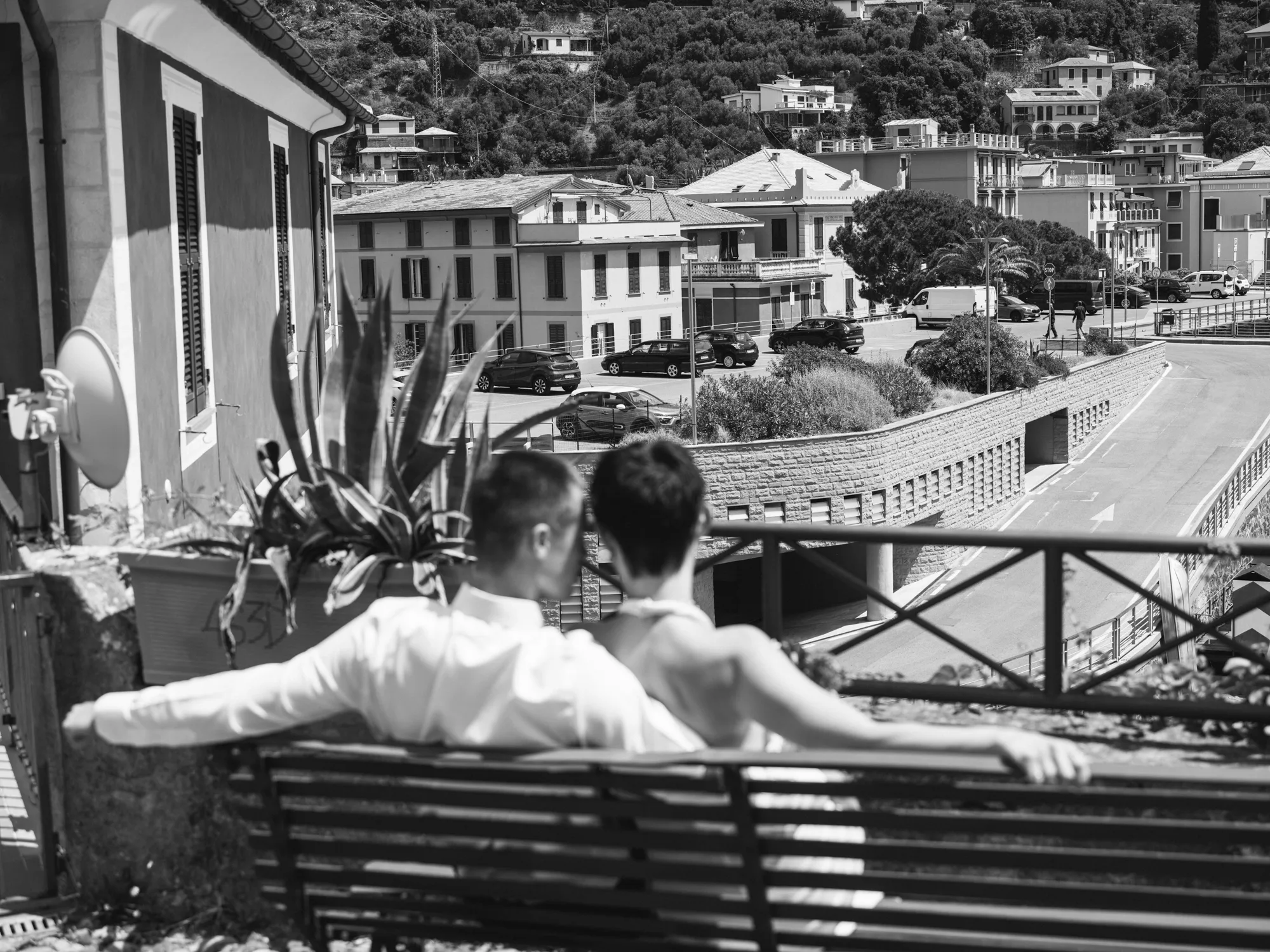 The photograph is in black and white, showing a couple sitting on a metal bench on a balcony in Bonassola