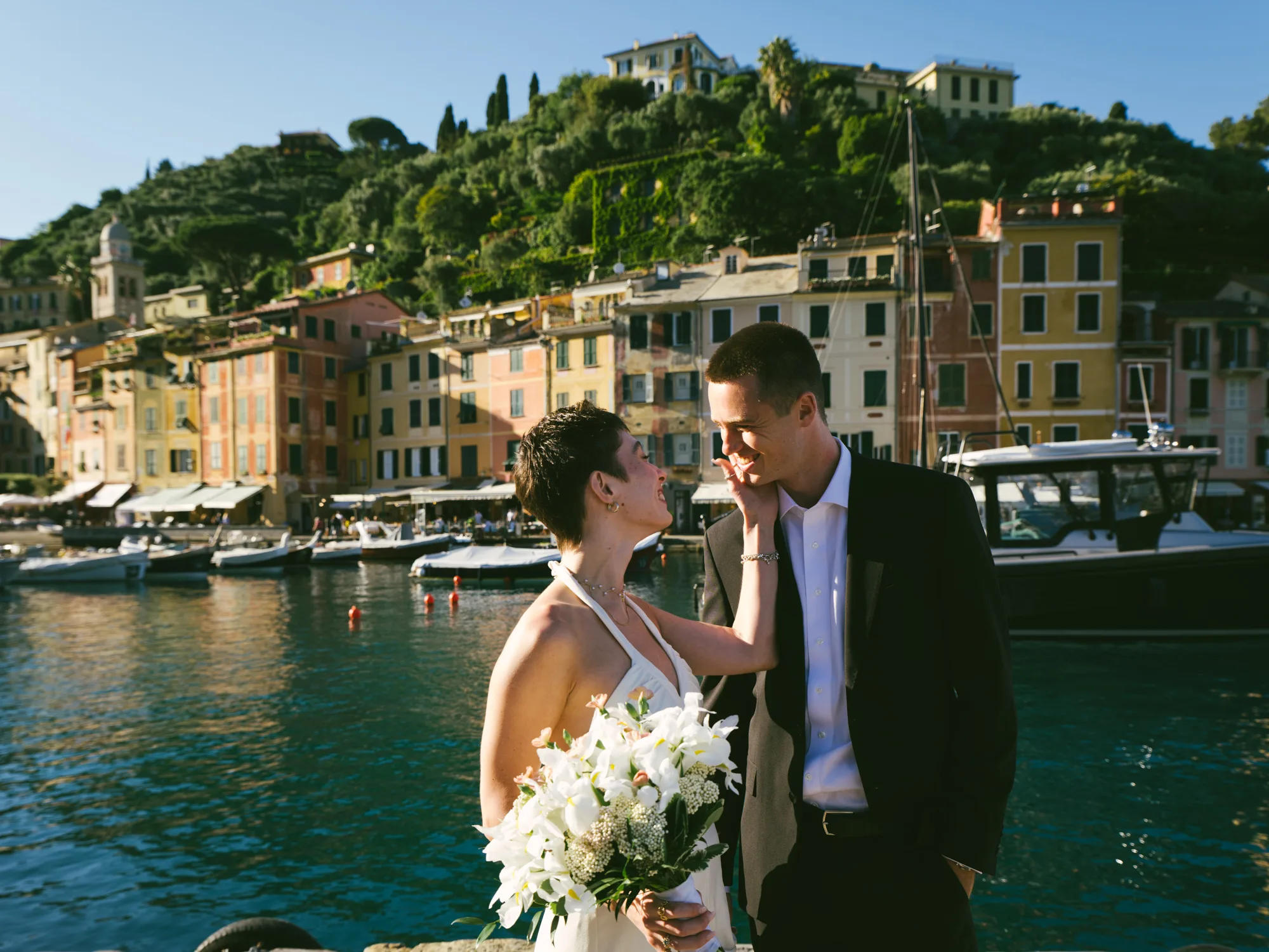 A bride and groom stand close together, the person holding a bouquet of white flowers in Portofino