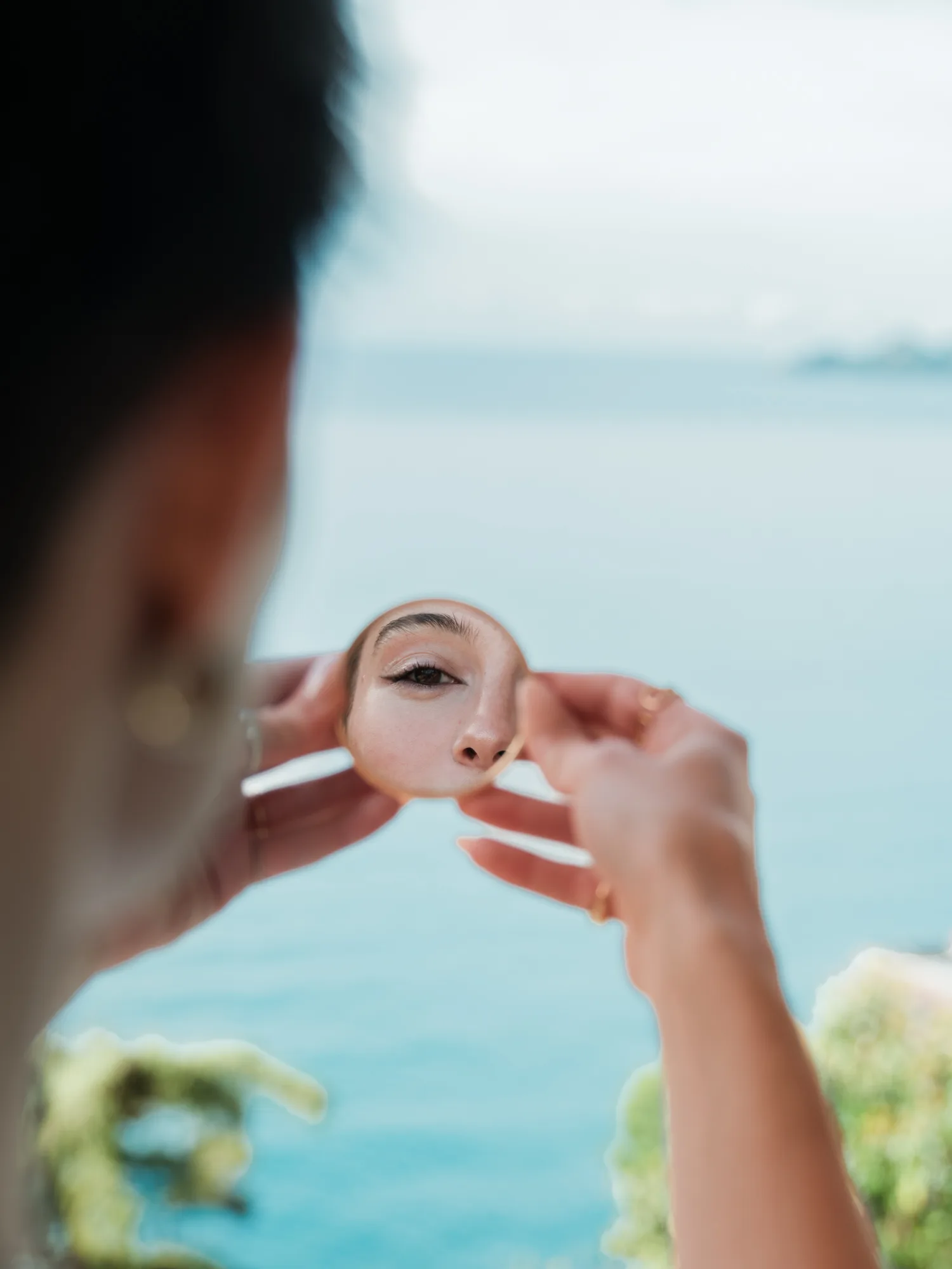 A bride is holding a small round mirror in front of their face, reflecting their eye.