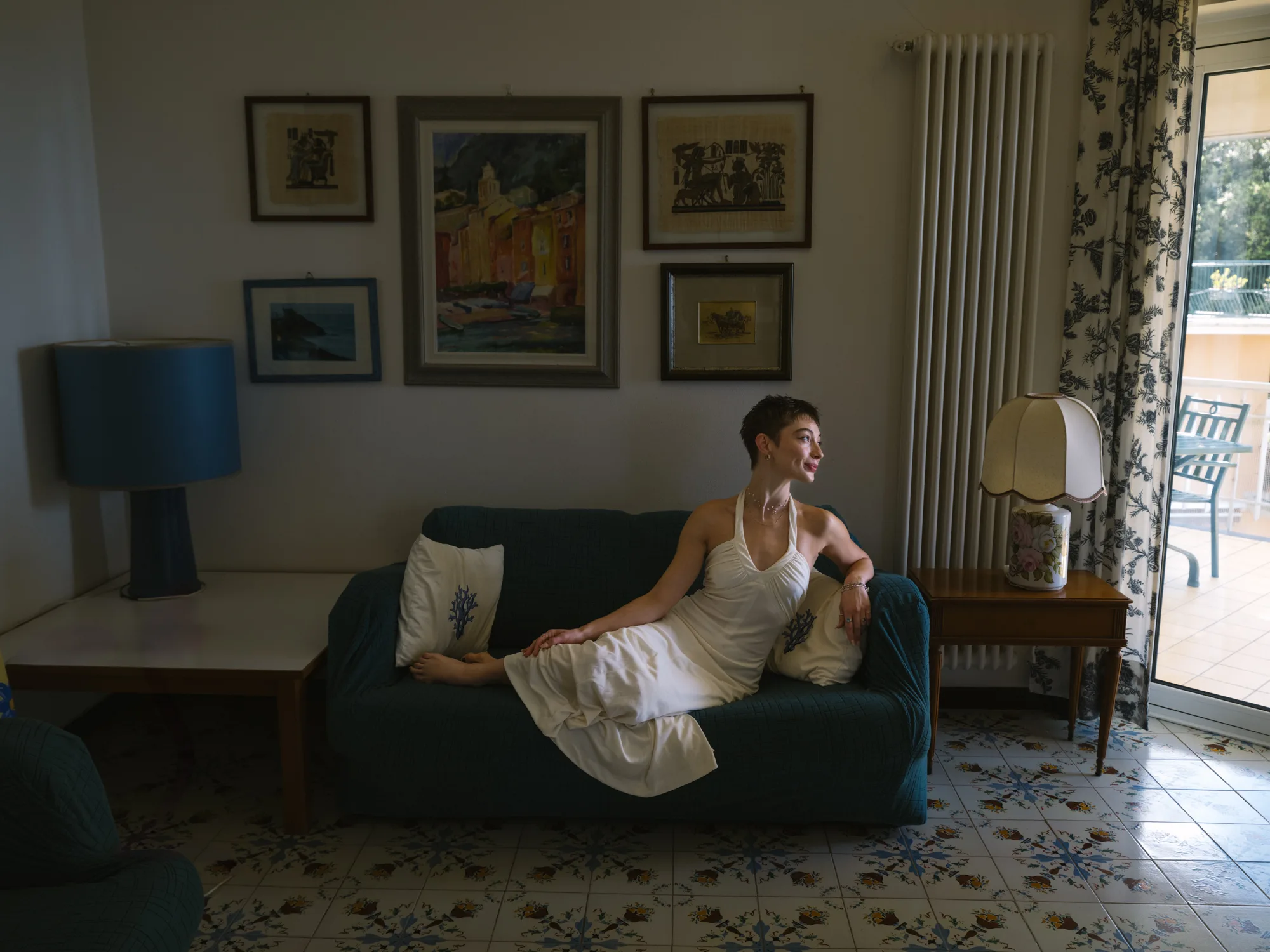 The bride in a white dress sits on a dark blue couch, leaning back against a white pillow.
