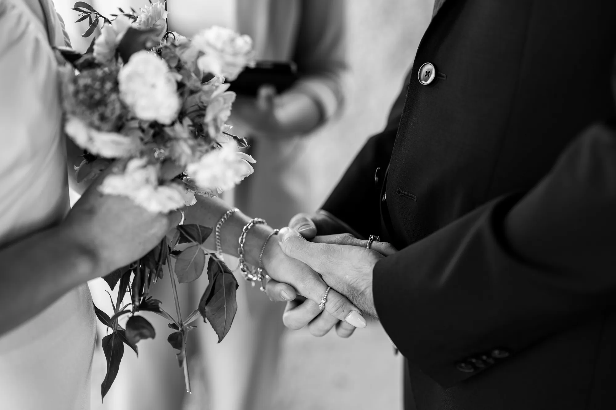 The photograph shows a close-up of two hands, one holding a bouquet of flowers and the other holding a ring.