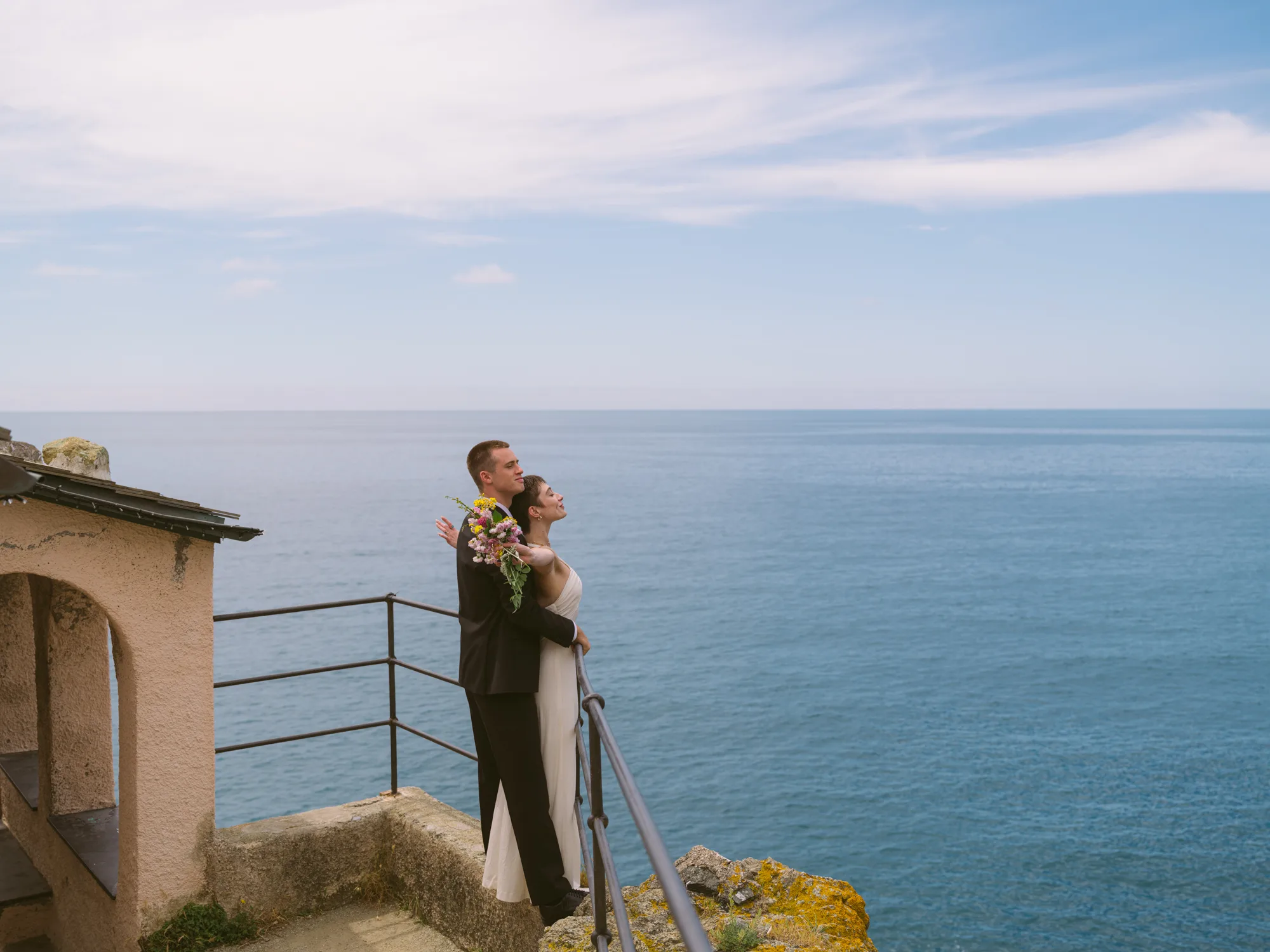 A couple is embracing on a balcony overlooking the ocean.