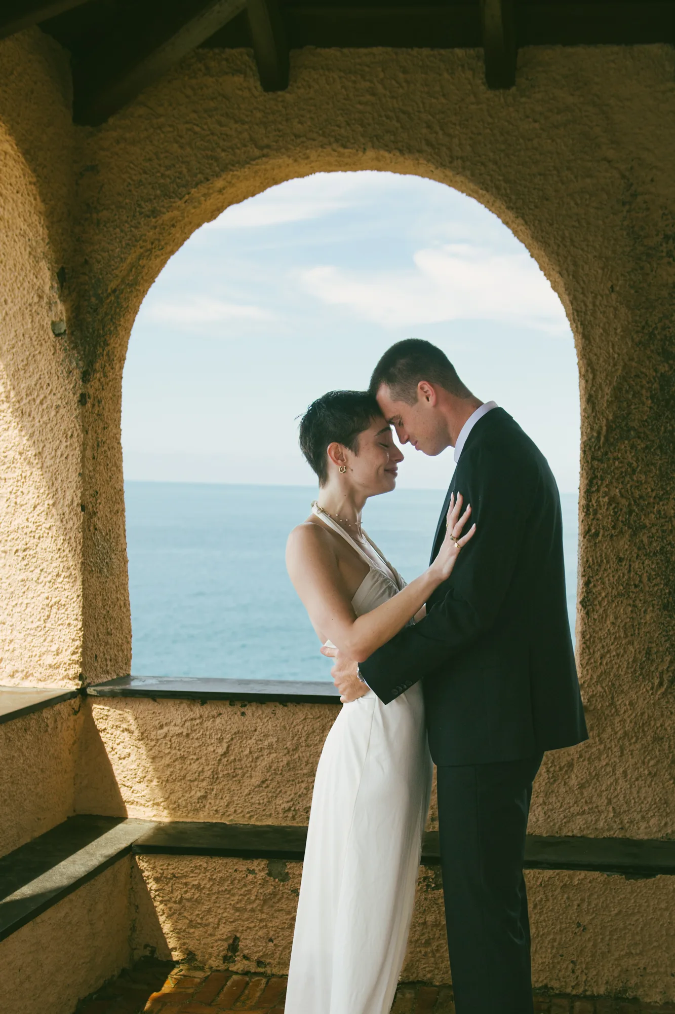 A couple is embracing in front of a window with a view of the sea