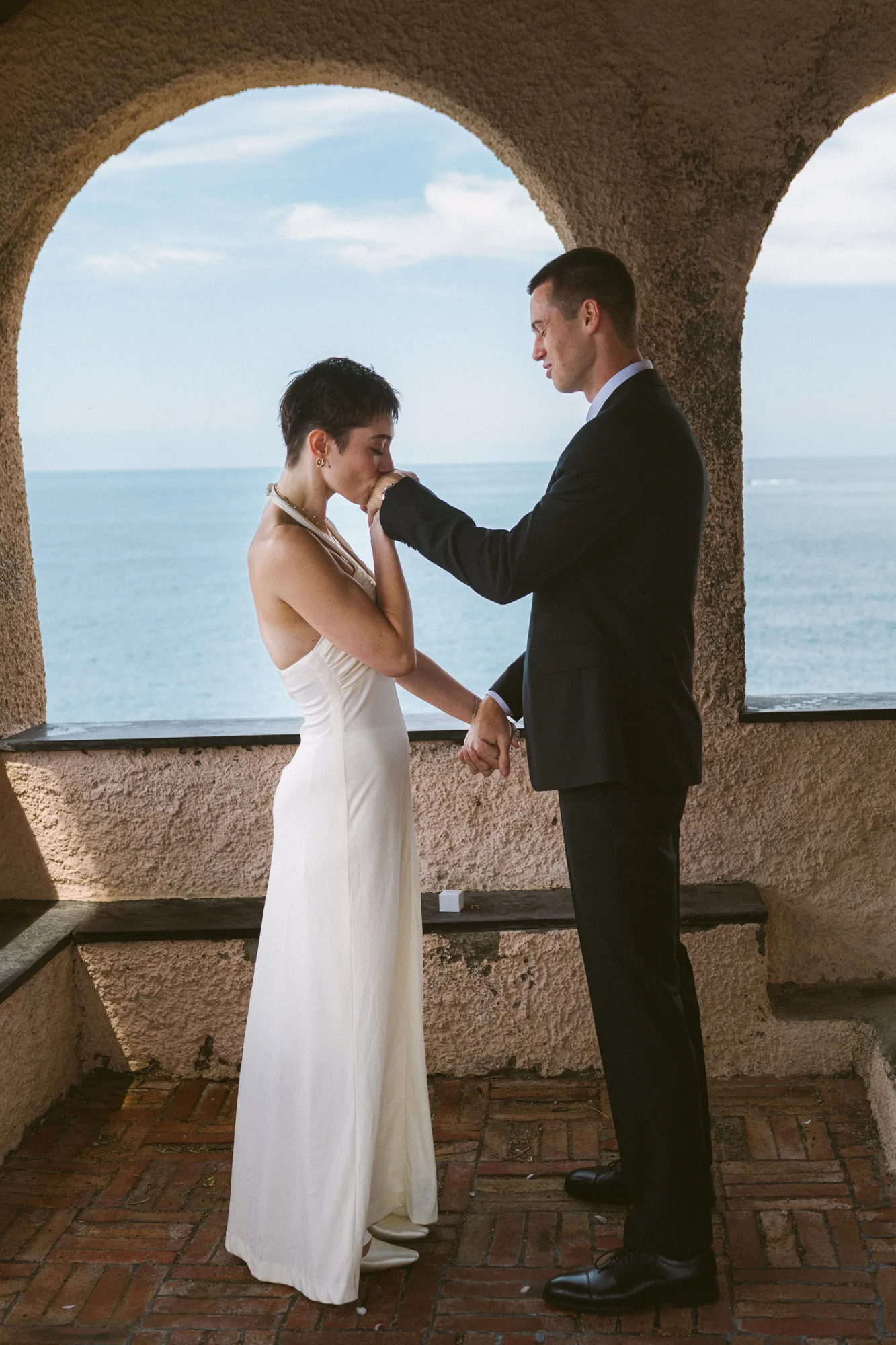 A couple stands under an archway, gazing at the sea.