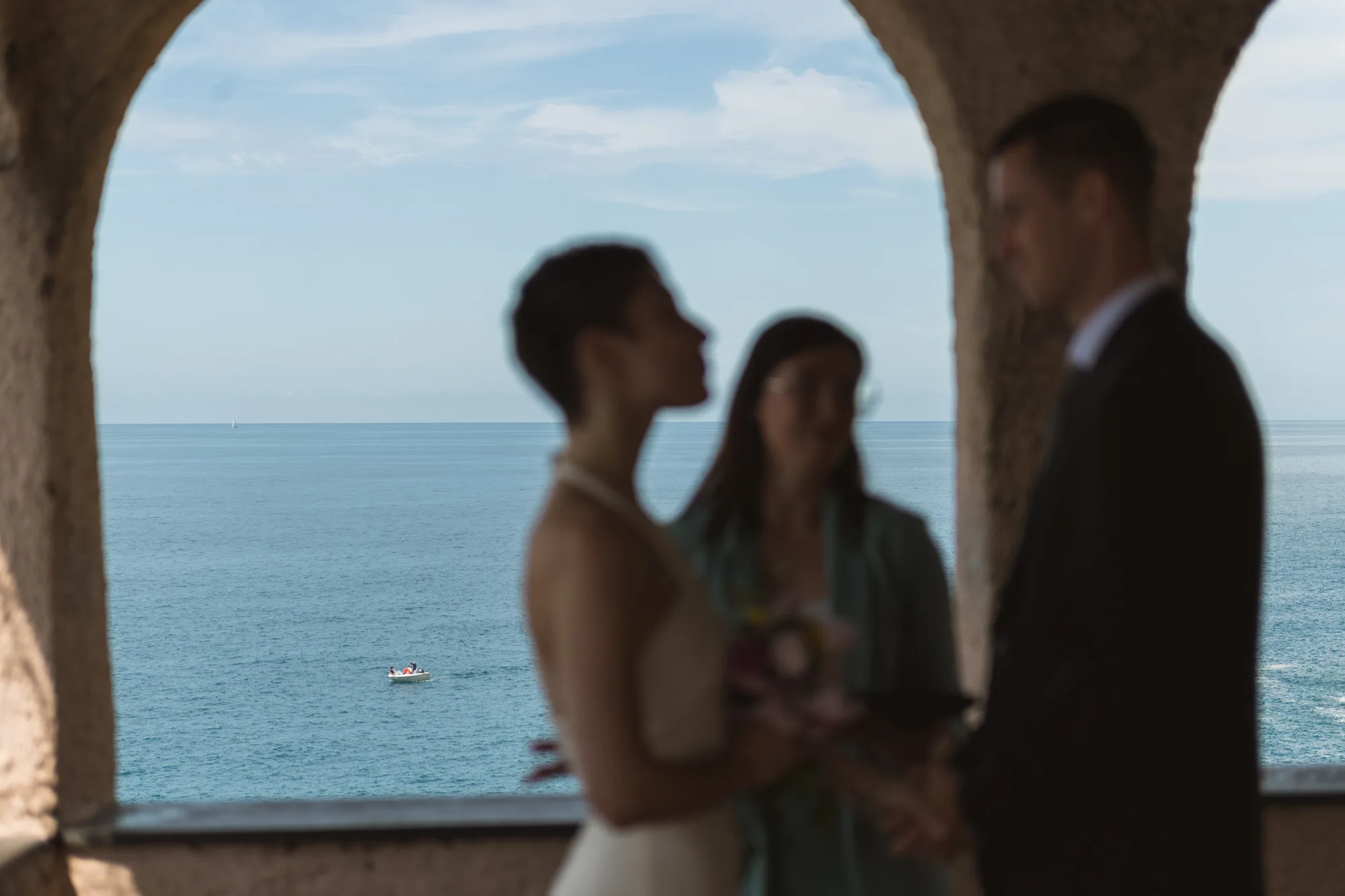 A couple stands under an archway, with the person in a white dress and the person in a dark suit.
