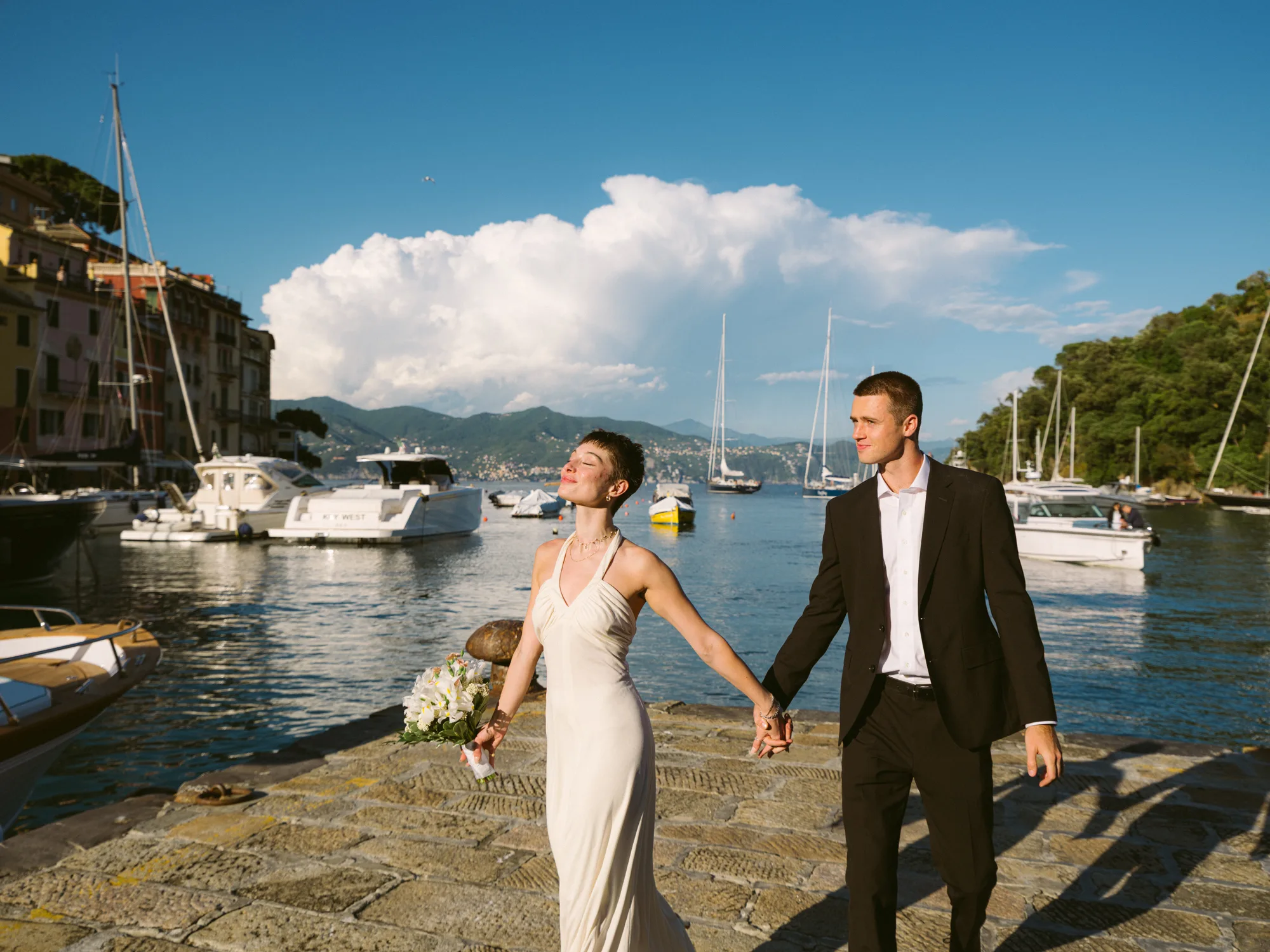 A couple is walking along a stone-paved path by the water, holding hands in Portofino