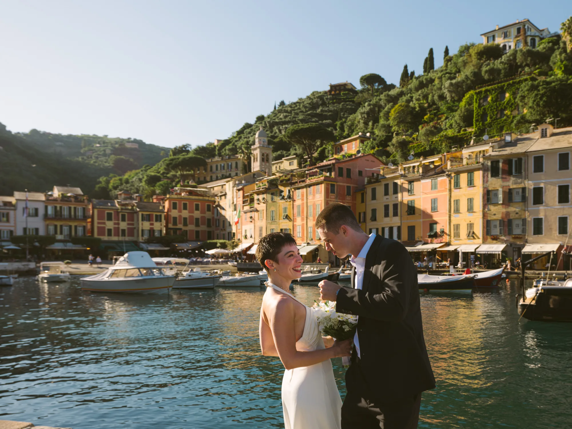 The photograph features a couple standing by a waterfront, with a picturesque town in the background in Portofino