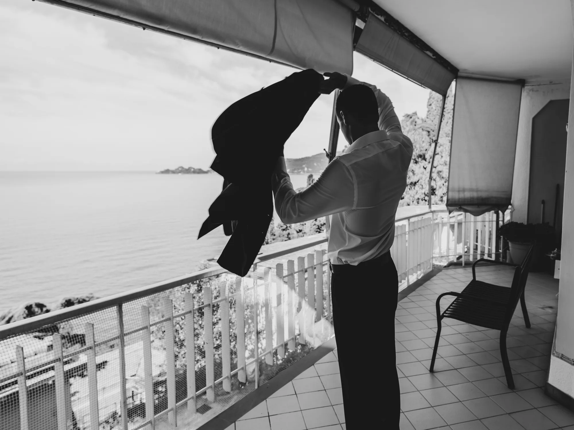 A groom is standing on a balcony, adjusting their hat.