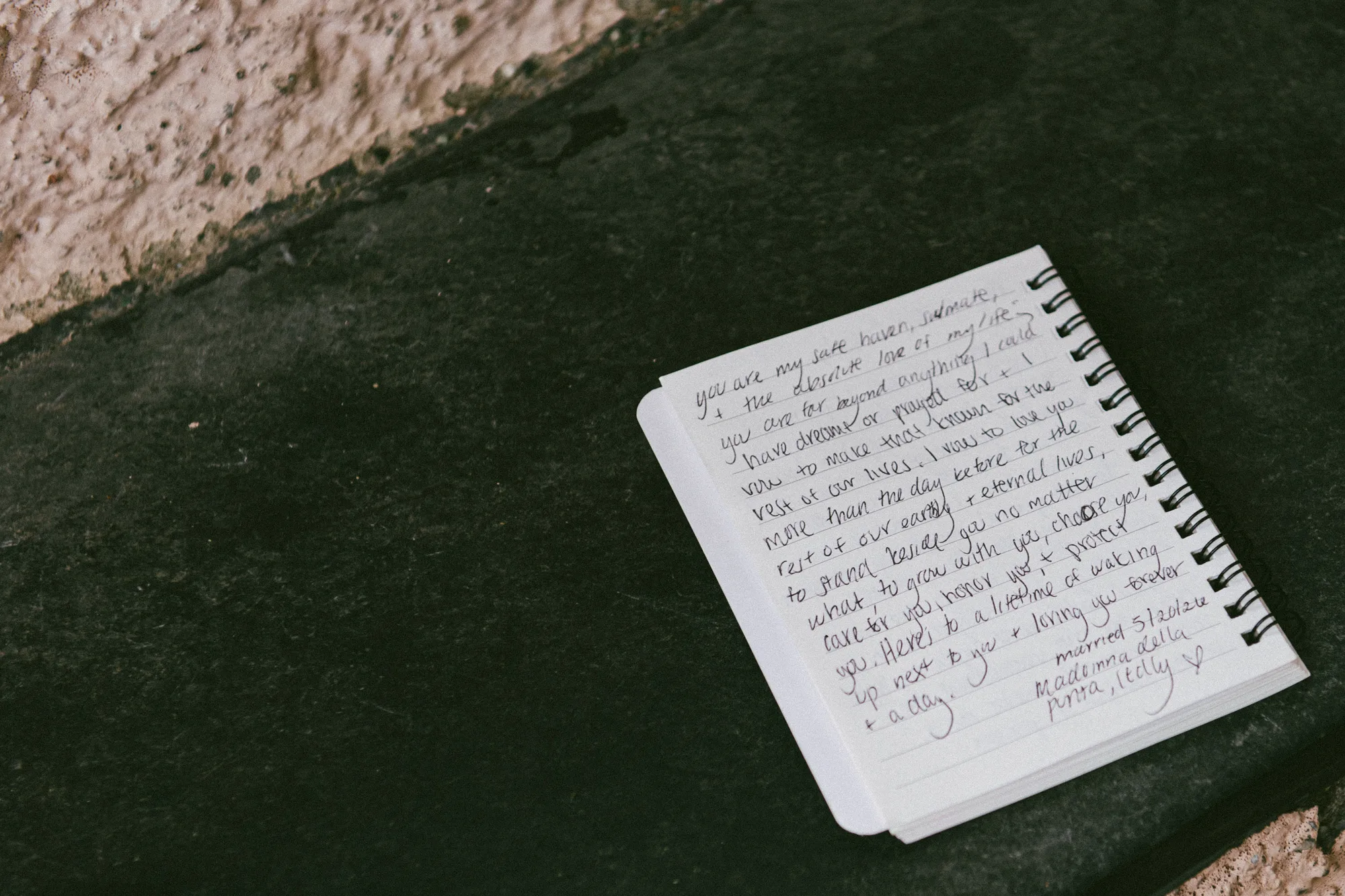 The photograph shows a handwritten wedding vows note on lined paper, placed on a textured surface.