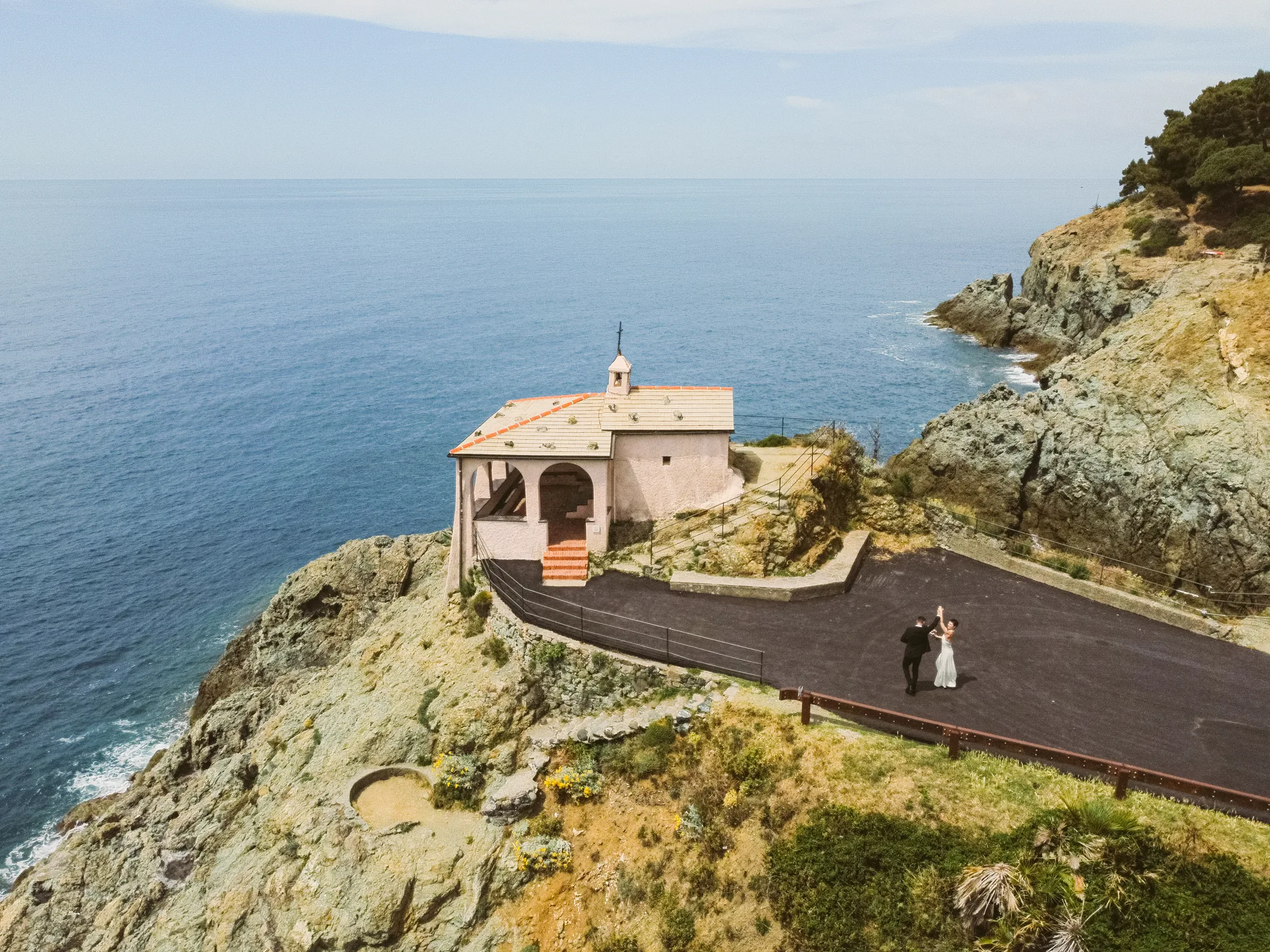 Haley and Daniel beside Cappella della Madonnina della Punta, a white cliffside wedding chapel overlooking the Mediterranean Sea in Bonassola, Italy.