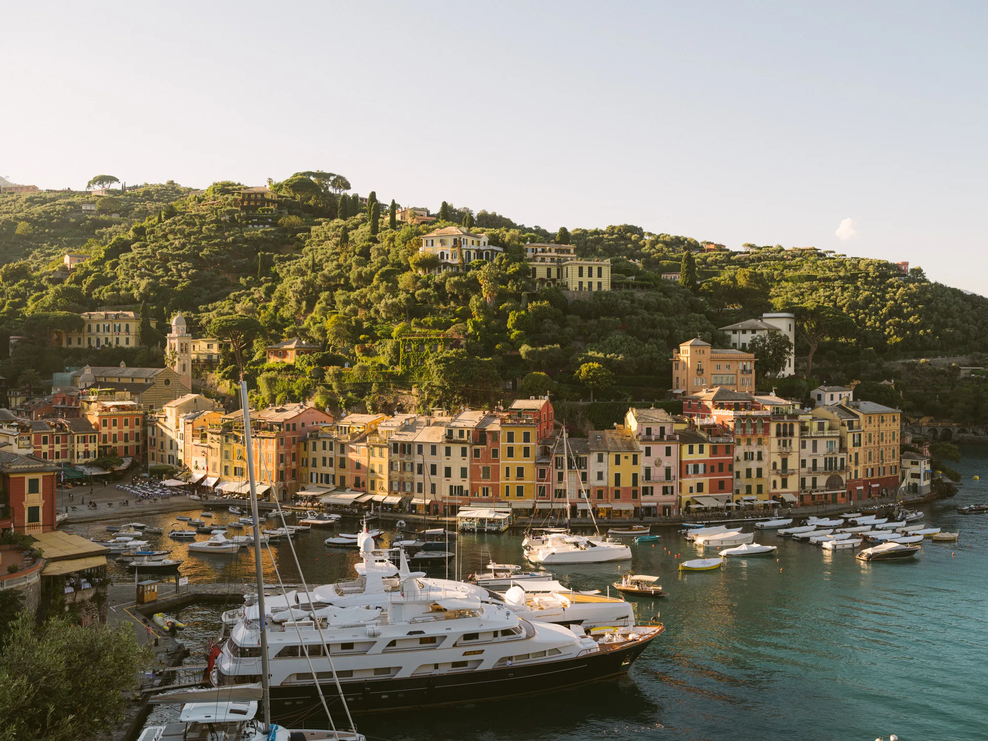 The photograph shows a picturesque coastal town with colorful buildings and a hillside covered in greenery.