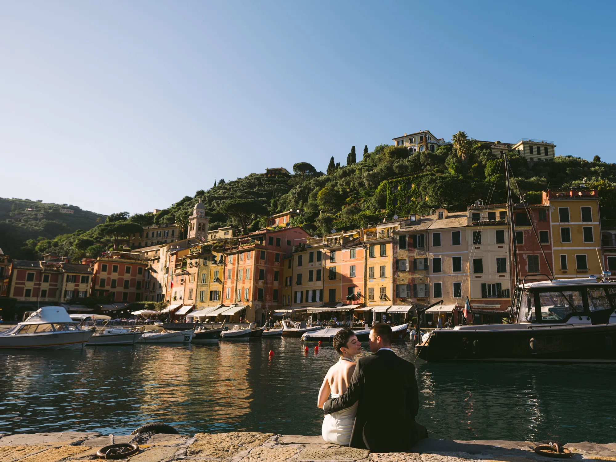The photograph shows a picturesque Portofino harbor with colorful buildings lining the waterfront, and a clear blue sky above.