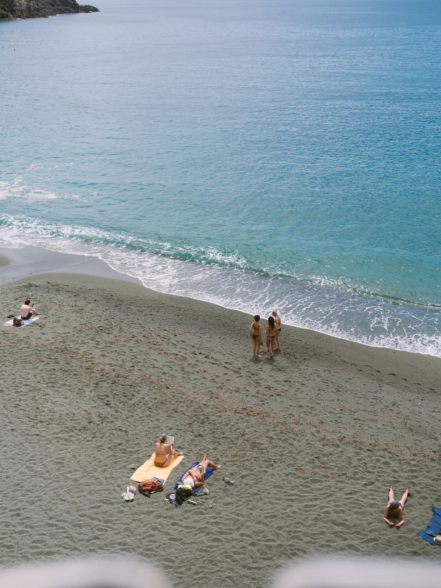 The photograph shows a sandy beach with several people enjoying the sun and sea.