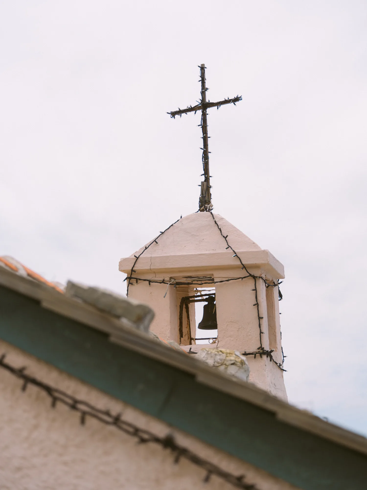 The photograph shows a small, light-colored bell tower with a cross on top.