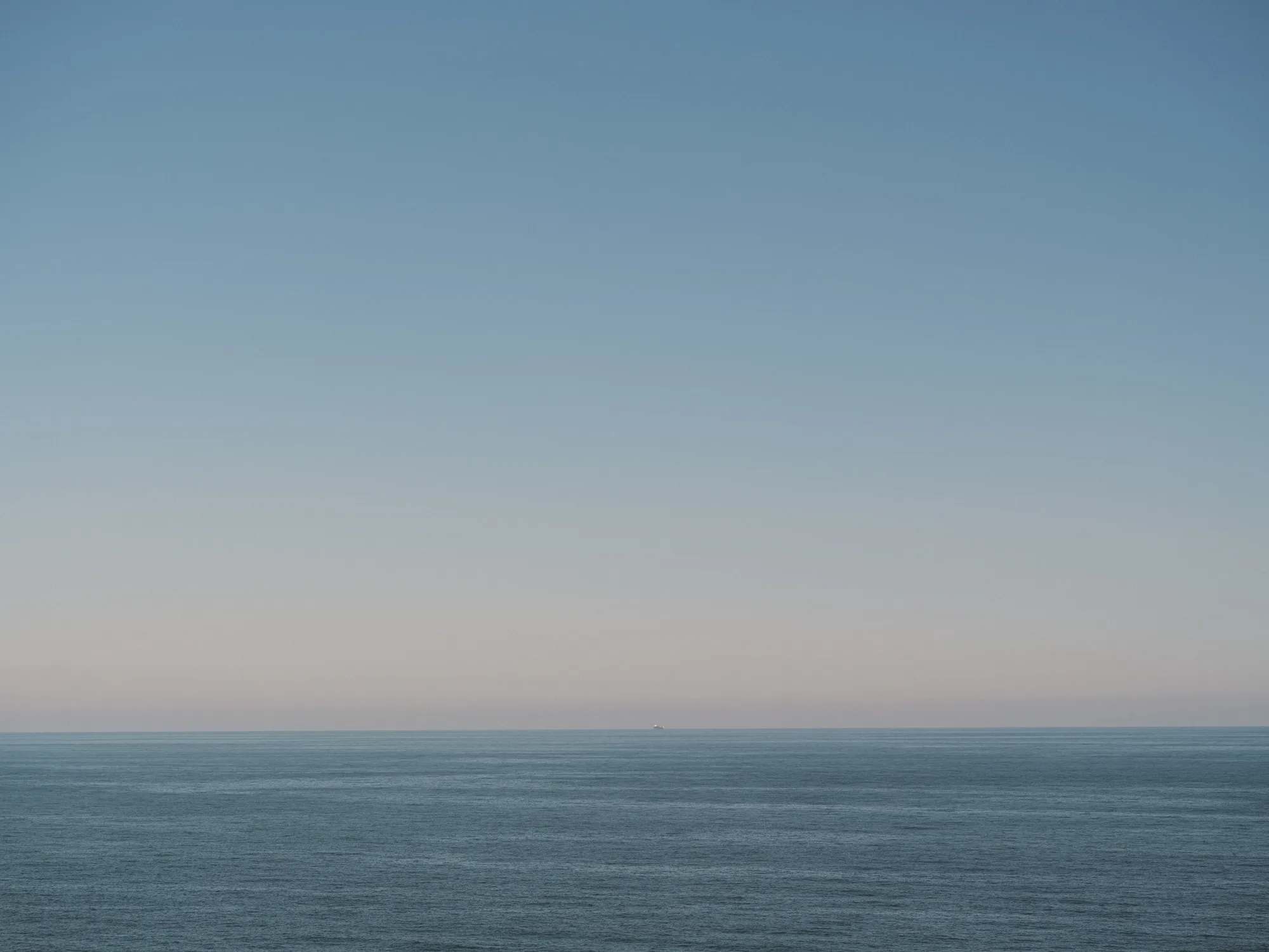 The photograph shows a vast expanse of calm, deep blue ocean stretching to the horizon under a clear, light blue sky.