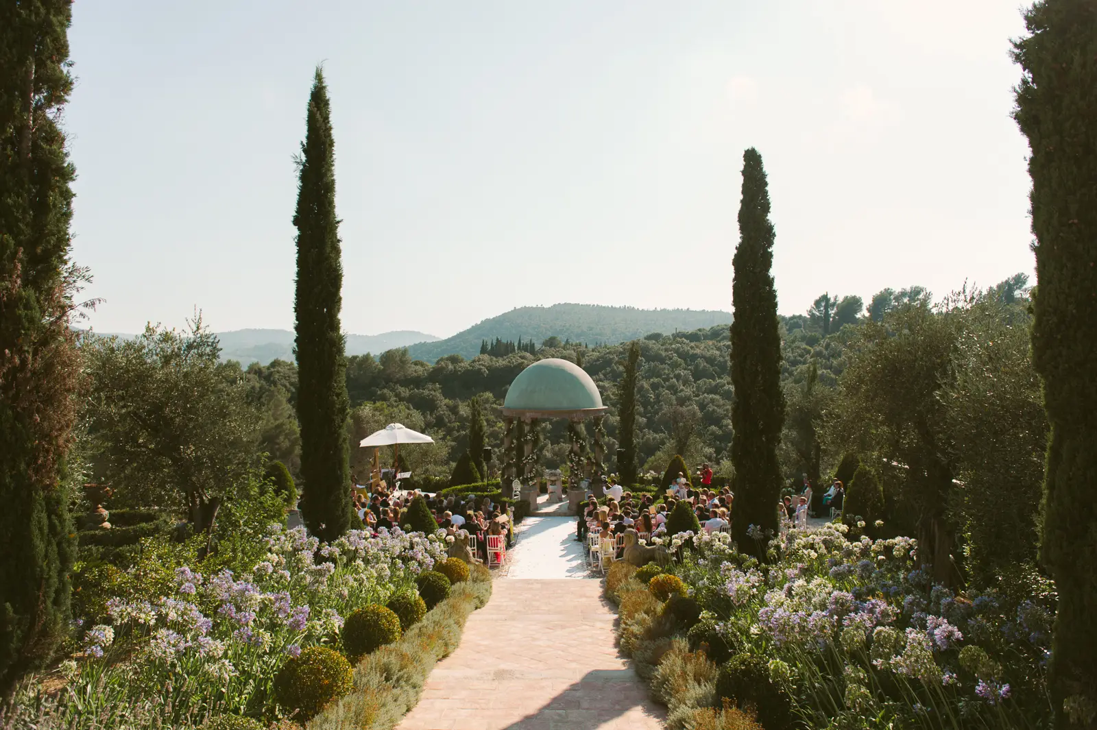 Outdoor ceremony at Château Diter under gazebo overlooking mountain tops, flowerbeds and southern evening light.