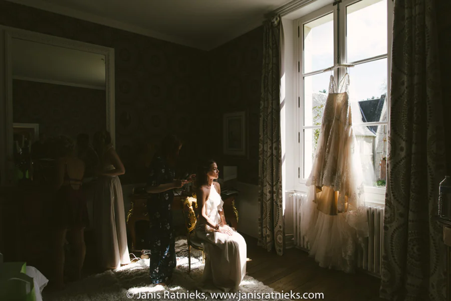 Bride silhouetted beside a château window before dressing