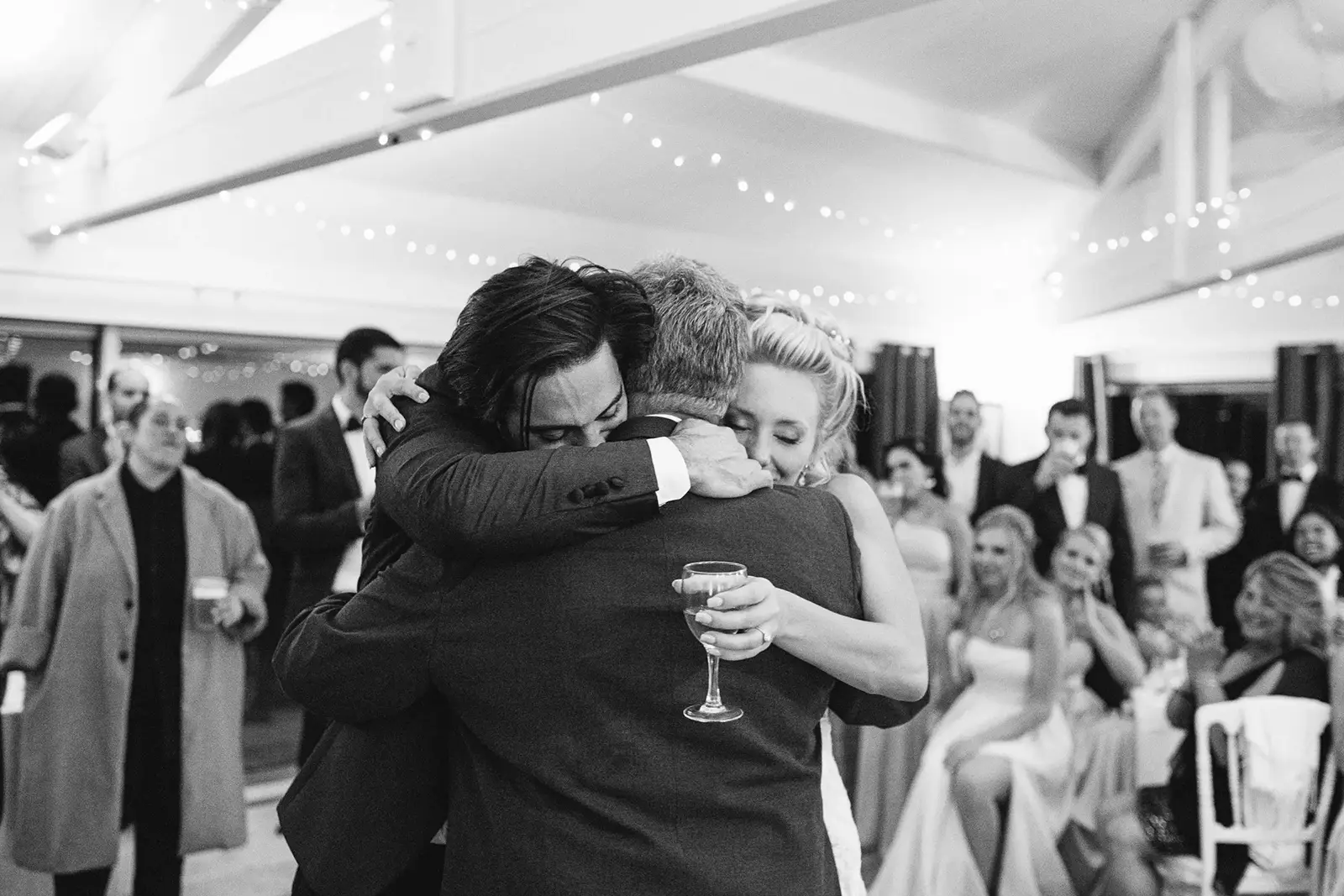 Black-and-white photograph of an emotional family embrace at a French Riviera wedding reception