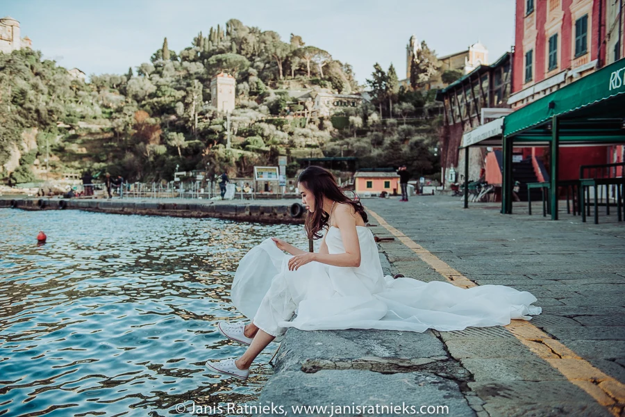 Bride seated on the harbour stones with Portofino rising behind her