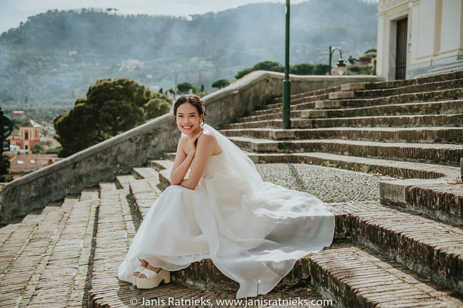 Bride seated on the stone steps with misty Ligurian hills behind her