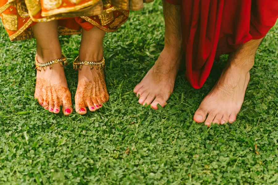 Hindu destination wedding photography, a very creative wedding image of bride and groom standing in grass, close-up with their feet, brides feet decorated with henna tattoo.