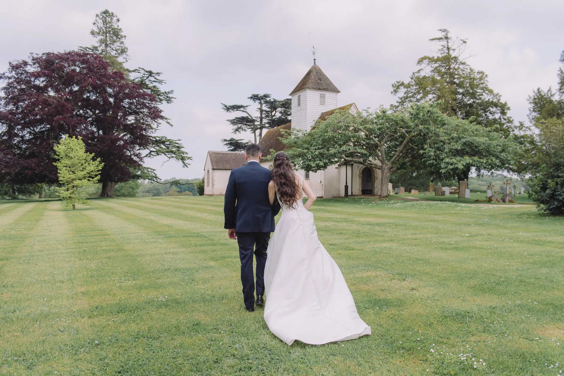 Bride and groom walking hand-in-hand through the scenic grounds of Wasing Park.
