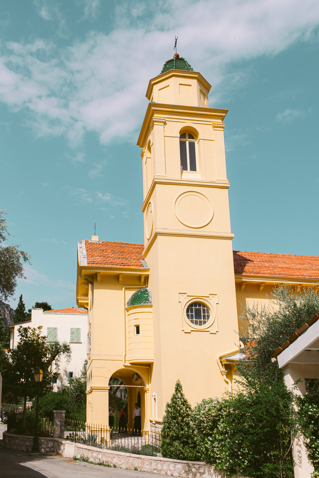 Newlyweds smiling as guests gather outside the yellow façade of St Michael’s church in Beaulieu-sur-Mer.