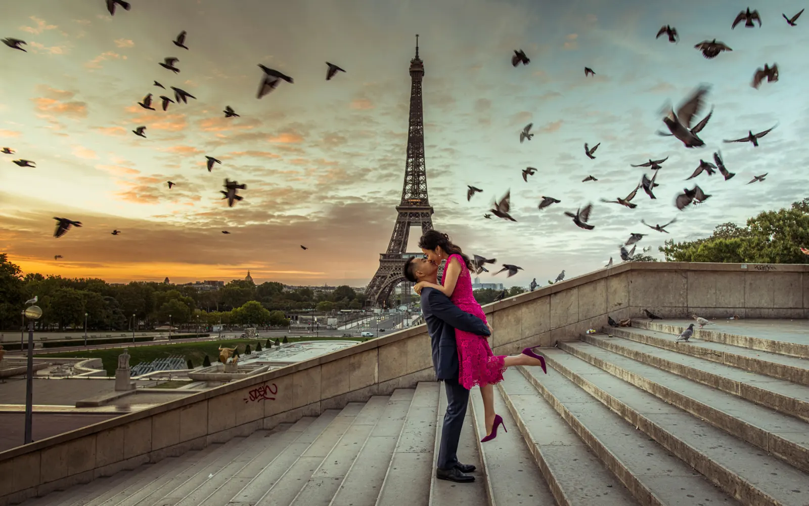 bride and groom in an epic photograph in front of Eiffel Tower during sunrise, skies full of doves, groom lifting bride un and kissing